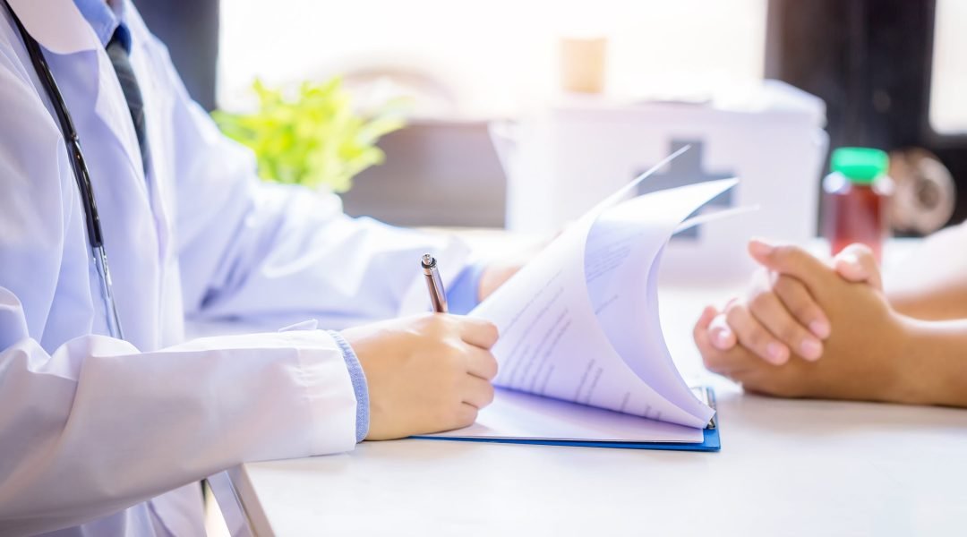 Doctor man consulting patient while filling up an application form at the desk in hospital. Medicine and health care concept